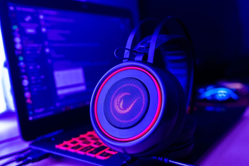 Gaming headset with neon lighting placed next to laptop on gaming desk