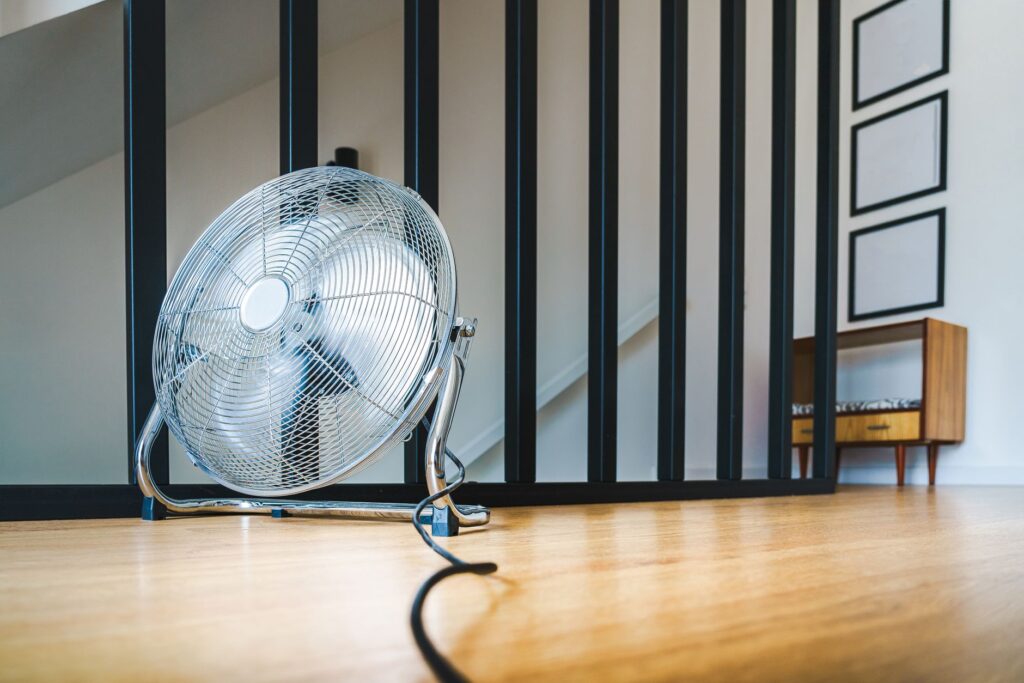 A sleek electric fan placed on a wooden floor in a modern indoor setting providing comfort and cooling