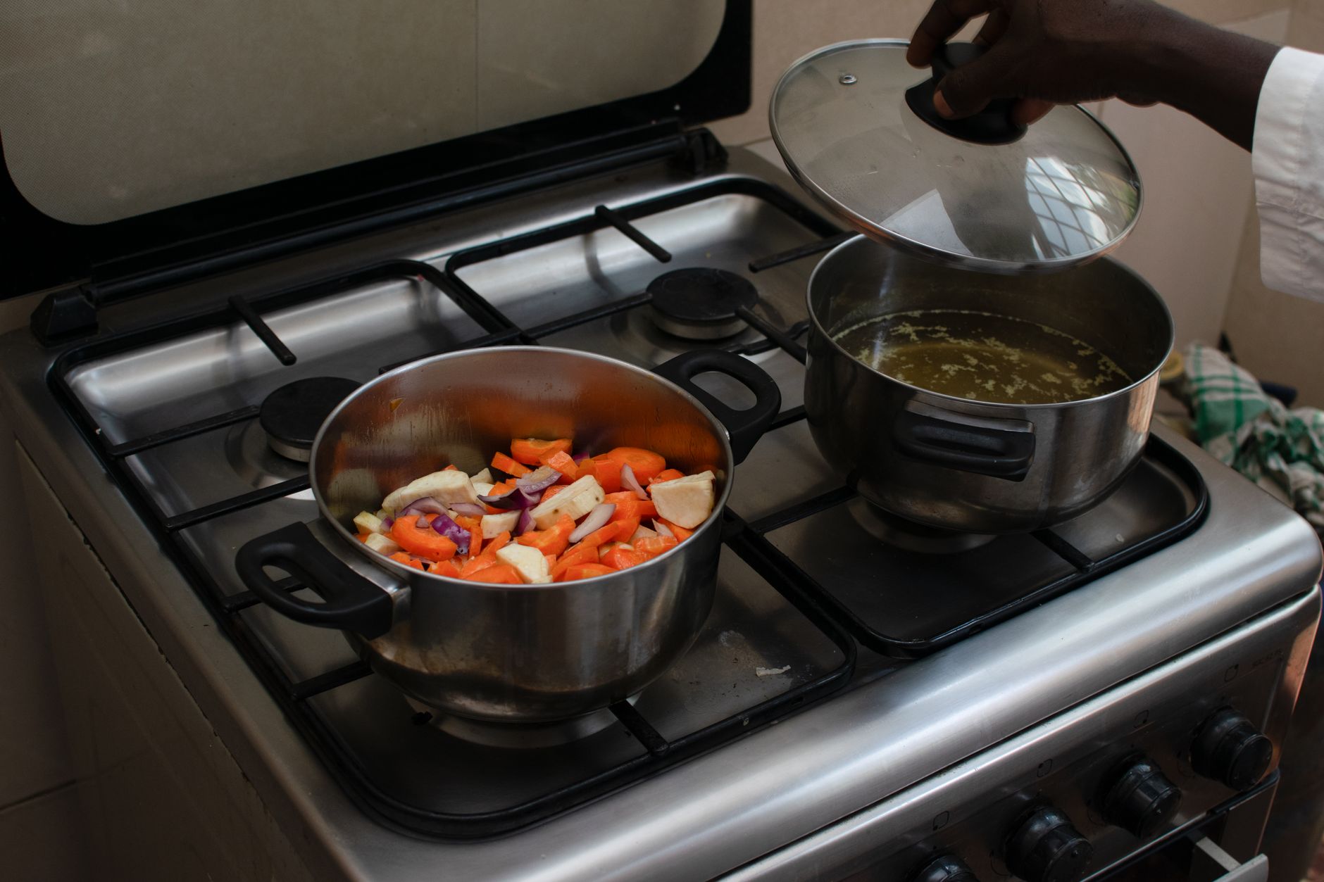 A kitchen scene featuring fresh vegetables being cooked in pots on a gas stove.