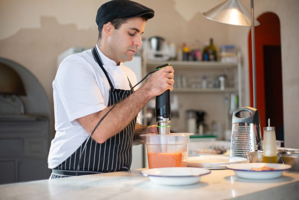 Chef blending ingredients with hand blender in modern kitchen