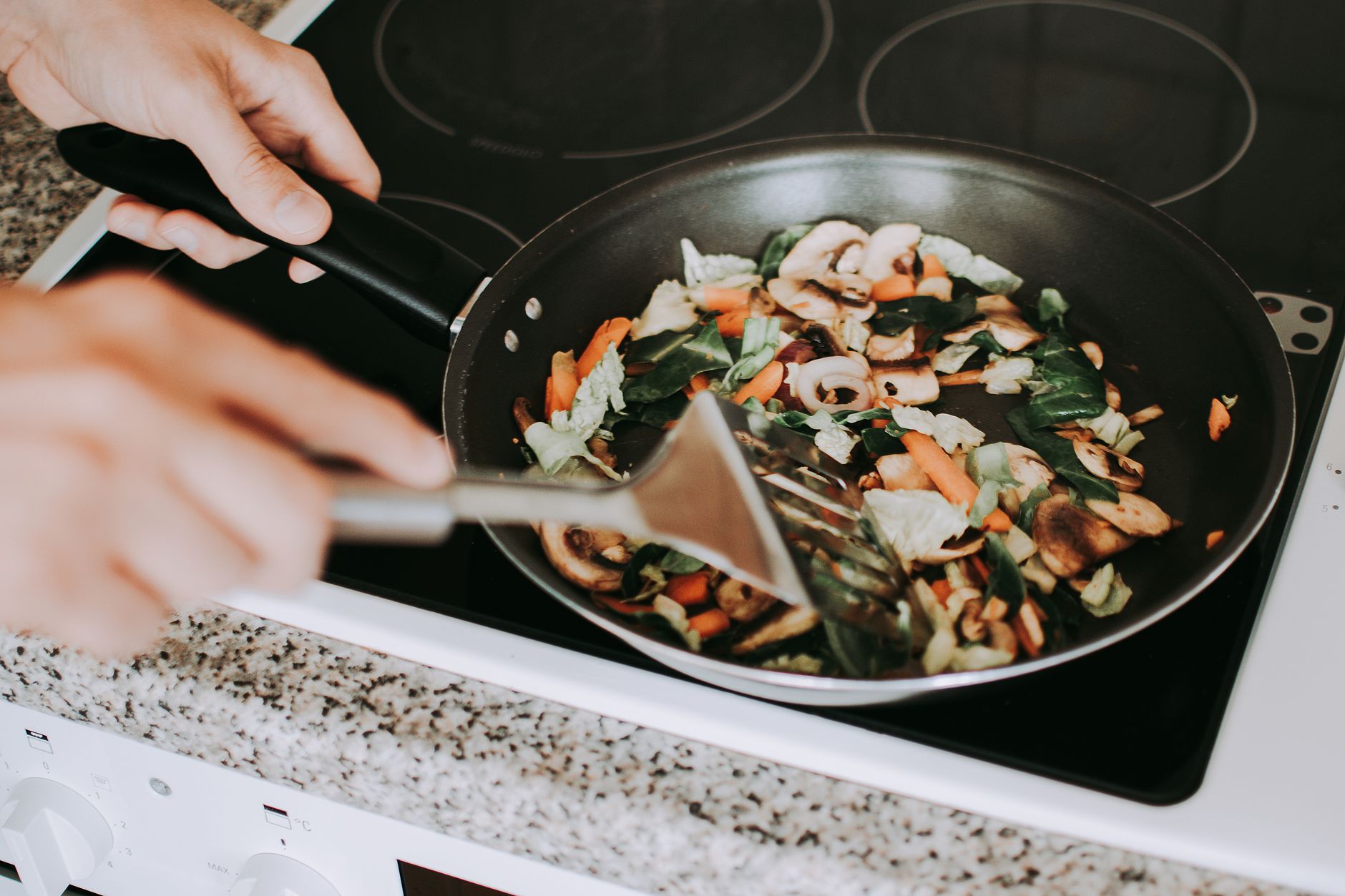 Stirring vegetables in non-stick frying pan on electric stove