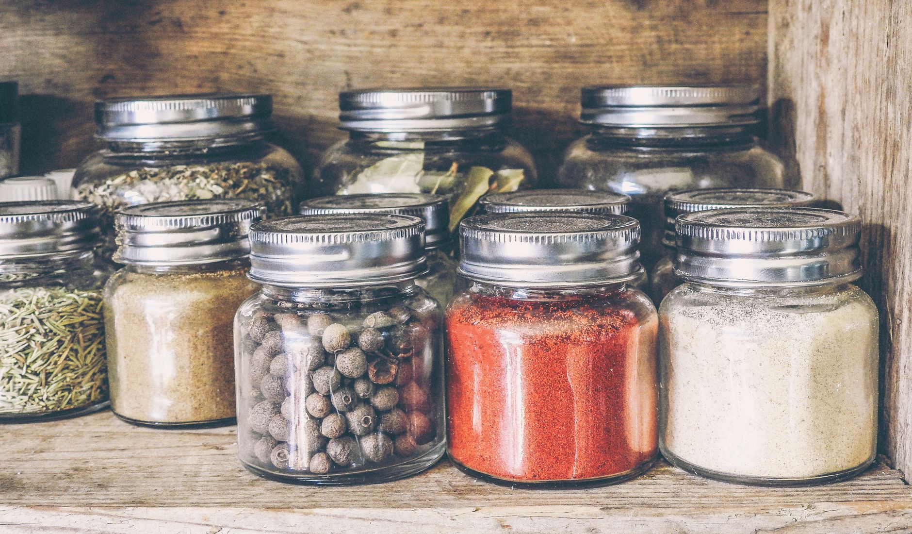 Glass spice jars with various Indian spices and herbs on wooden kitchen shelf for organised storage