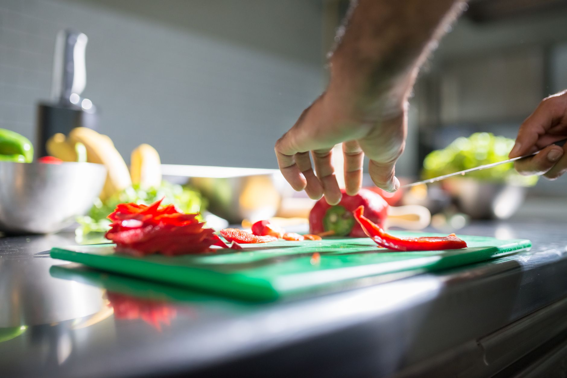 Hands slicing fresh red bell pepper on a chopping board in an Indian kitchen