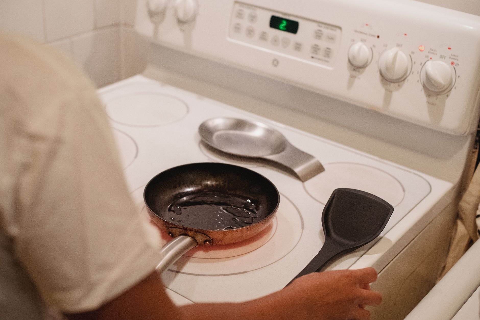 Woman cooking food in a non-stick pan on a white stove in an Indian kitchen