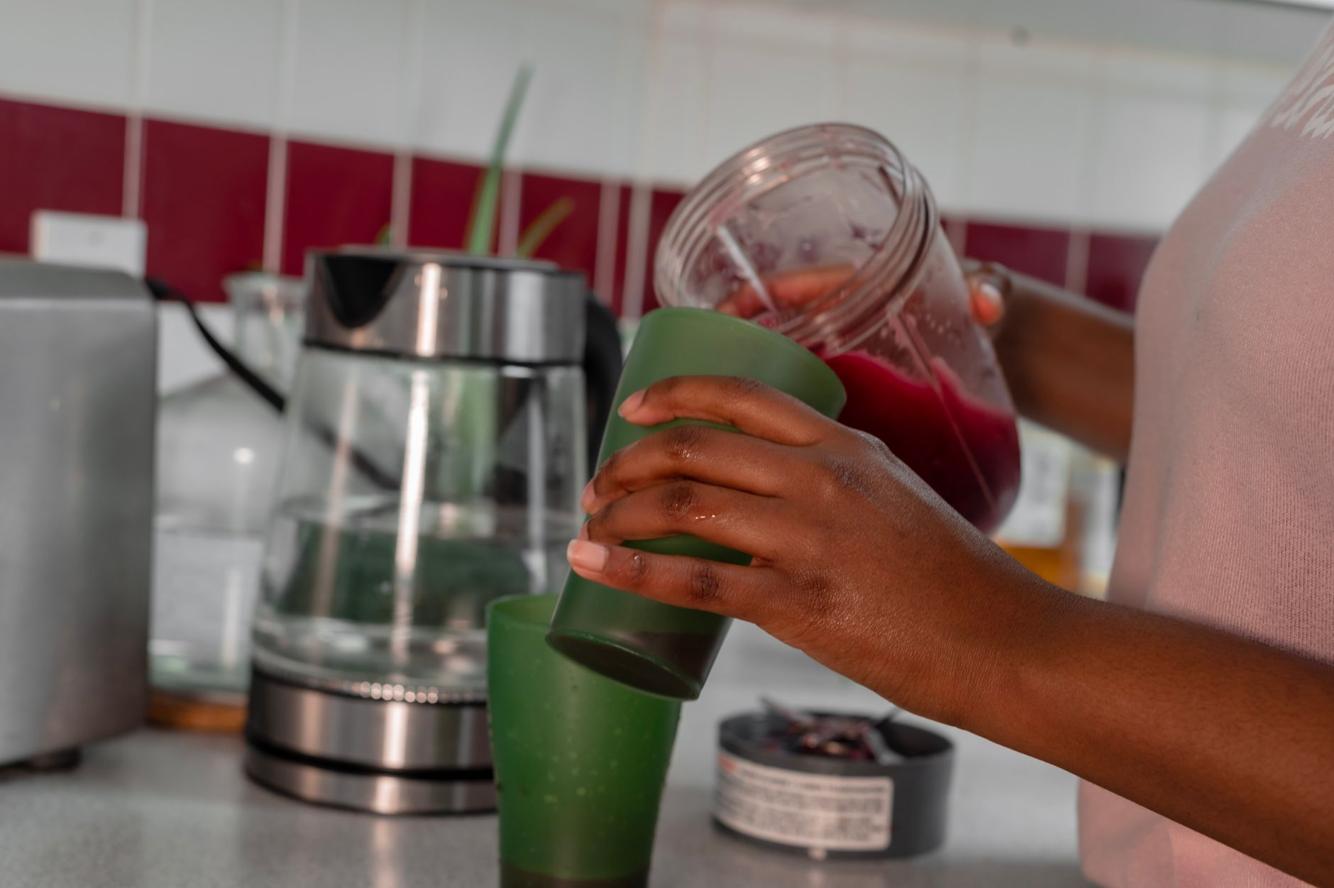 Person pouring fresh juice from blender cup in kitchen with juicer appliance on counter