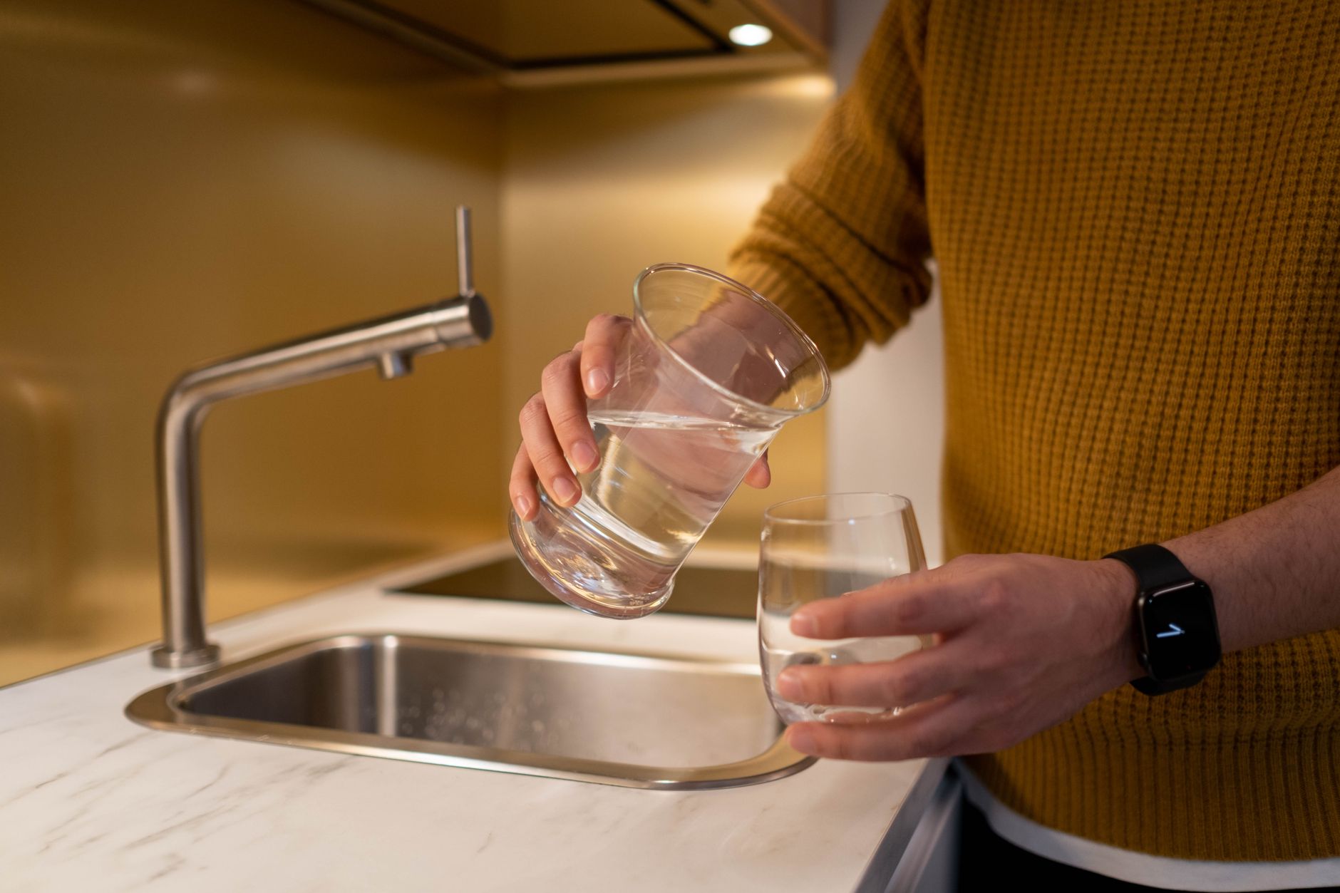 Pouring purified water into glass in modern kitchen